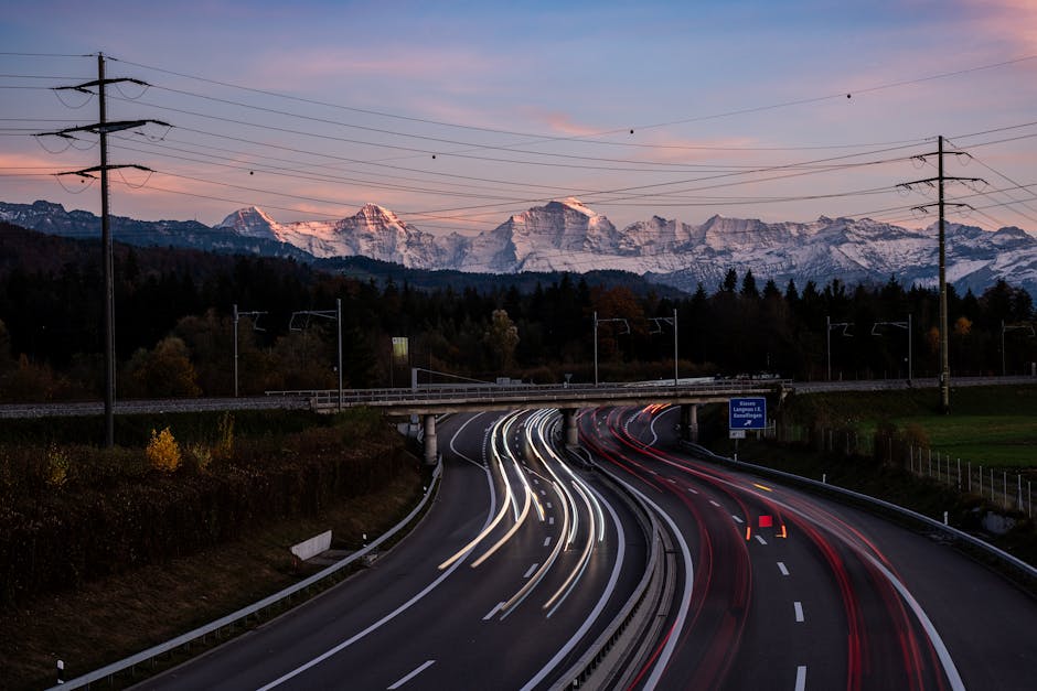 Dynamic long-exposure highway scene with Swiss Alps backdrop at dusk in Bern, Switzerland.