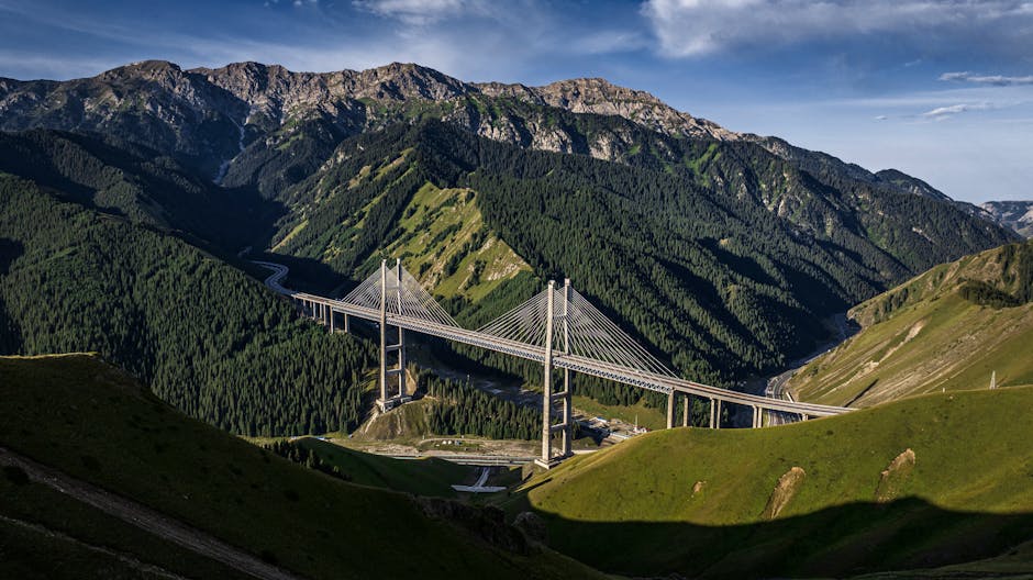 Scenic aerial view of the Guozigou Bridge amidst lush greenery and mountains in Xinjiang, China.